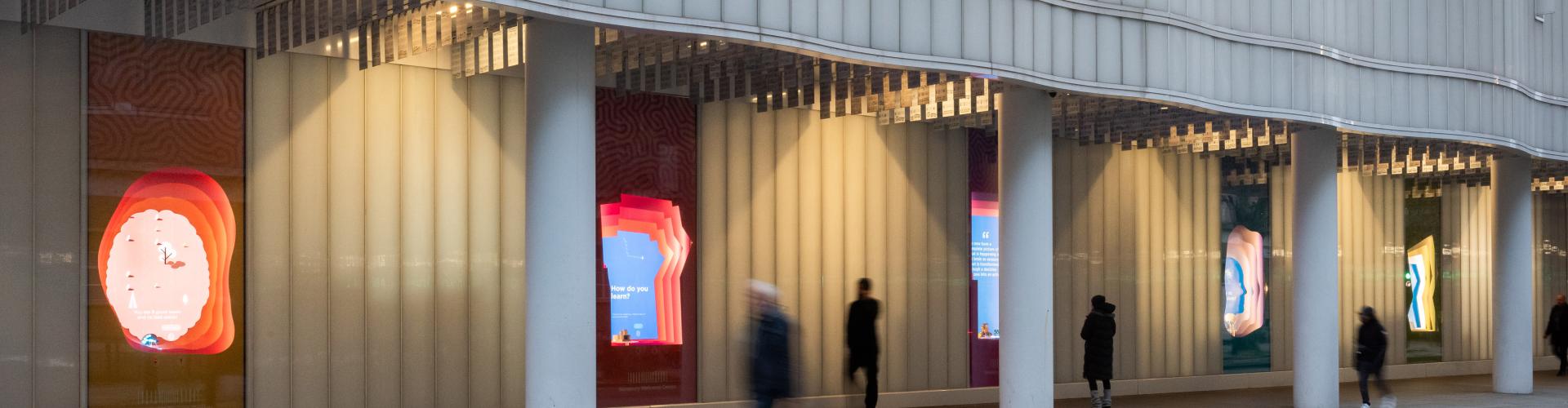 Photo of the five window displays outside the SWC building on Howland Street with people passing by