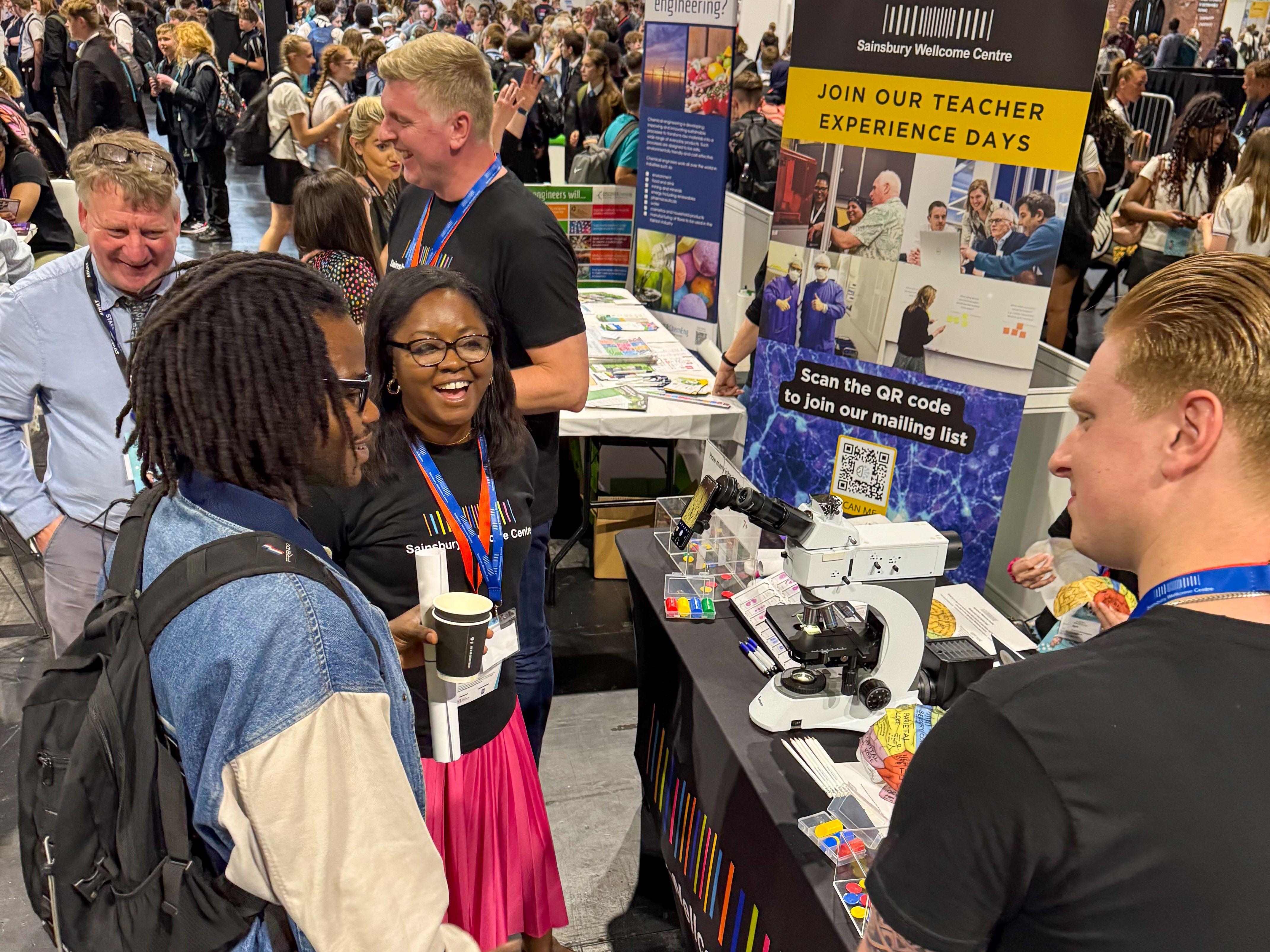 Photo of SWC volunteers with educators at the Big Bang Fair 2025 at an exhibition stand with banners, brain hats and a microscope.