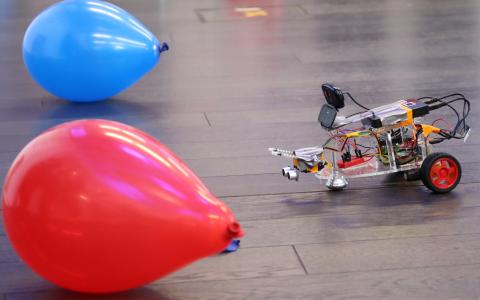 A photo of a robot, built by SWC students, hesitating between a red and a blue balloon