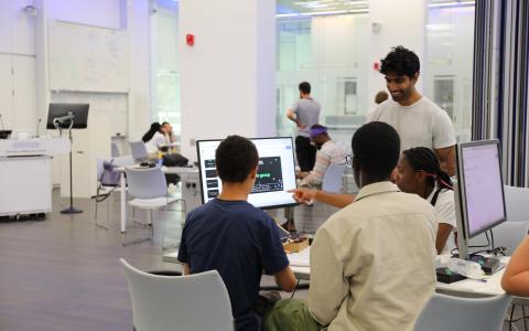 Three students and a teacher gathered around a computer during the Neuronauts summer camp